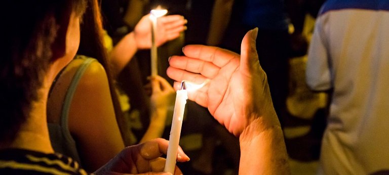 People holding candle vigil in darkness seeking hope, worship, prayer